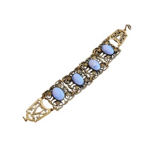 Puede incluir: Un brazalete de oro con un delicado diseño de filigrana y cuatro piedras ovaladas de color azul claro.