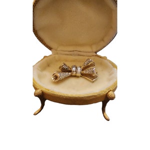 May include: A gold bow brooch with clear rhinestones, displayed in a gold velvet-lined box with three legs.
