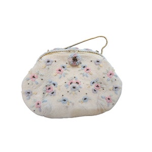 Puede incluir: Un bolso de noche blanco de cuentas con un diseño floral en tonos rosa y azul. El bolso tiene un cierre dorado y un asa de cadena dorada.