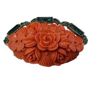 May include: A coral colored carved flower brooch with green rhinestone accents.