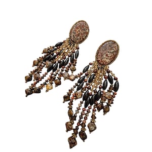 May include: A pair of dangle earrings featuring oval-shaped, speckled brown stones at the top. The earrings have multiple strands of brown, black, and clear beads, creating a cascading effect. The metal setting has a gold tone.