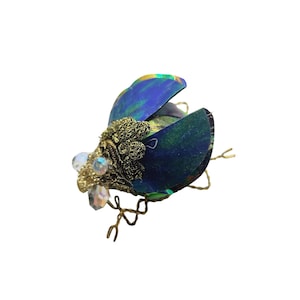 Könnte beinhalten: Ein blauer und grüner Käfer-Anhänger mit goldenen Akzenten und schillernden Flügeln. Der Käfer hat einen Drahtkörper und ist mit klaren Perlen verziert.