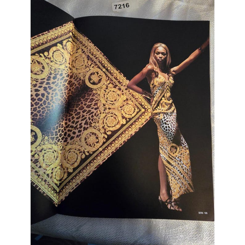 May include: A long, elegant dress with a gold and black pattern, featuring a leopard print and ornate gold detailing. The dress is worn by a person, and a matching scarf is draped behind them. The background is black.