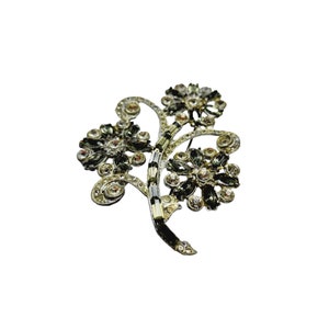 Könnte beinhalten: Eine silberfarbene Brosche mit drei Blumendesigns. Die Blumen bestehen aus klaren und dunkelgrünen Strasssteinen.