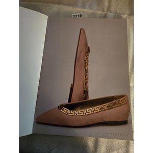 May include: A pair of blush-colored ballet flats with a gold-toned chain detail around the topline. The shoes are displayed on a gray background, with one shoe upright and the other flat. The word "SIGNATURE" is printed at the bottom.