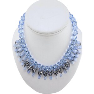 May include: A light blue crystal beaded necklace with a graduated design. The necklace features a row of larger crystal beads with smaller crystal beads dangling from the bottom.