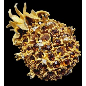 May include: A gold-toned brooch in the shape of a pineapple with a cluster of brown and clear rhinestones.