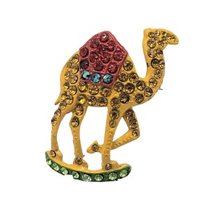 May include: A yellow jeweled camel brooch with a red, blue, and green jeweled saddle.