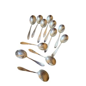 May include: A set of silver spoons, each with an oval bowl and a long, thin handle. A small emblem is visible near the bowl of each spoon. The spoons are displayed against a white backdrop, suitable for dining.