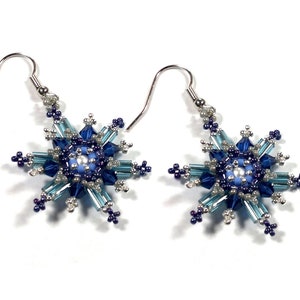 Puede incluir: Un par de pendientes de copo de nieve plateados con cuentas azules y blancas.