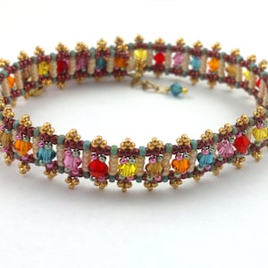 Pode incluir: Um bracelete de contas coloridas com detalhes dourados. O bracelete apresenta uma variedade de contas pequenas e facetadas em tons de vermelho, laranja, amarelo, verde, azul e rosa. As contas estão dispostas em um padrão repetitivo, criando um design visualmente atraente.