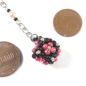 May include: A silver chain necklace with a pink and black beaded charm. The charm is about the size of a US penny.
