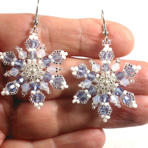 May include: A pair of snowflake earrings made with white and light blue beads. The earrings are silver and have a dangling design.