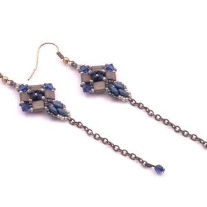 Op de afbeelding: Een paar lange zilveren kettingoorbellen met blauwe en grijze kralenaccenten. De oorbellen hebben een geometrisch, ruitvormig ontwerp.