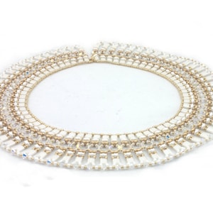 Op de afbeelding: Een witte en gouden kralenketting met een gelaagd ontwerp. De ketting is gemaakt van kleine, rechthoekige kralen en heeft een delicate, vrouwelijke uitstraling.