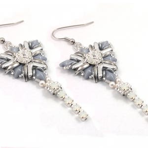 May include: A pair of silver earrings with a gray and white geometric design. The earrings feature a dangling chain of white beads.