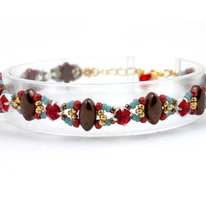 Peut inclure: Un bracelet en perles brun, rouge et bleu avec un fermoir doré. Le bracelet est sur un présentoir transparent.