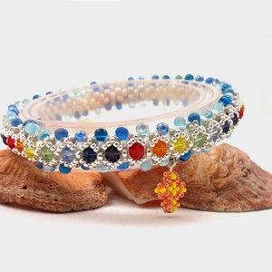 May include: A colorful beaded bracelet with a flower charm. The bracelet is made with blue, green, yellow, orange, red, and silver beads. The charm is orange and yellow.