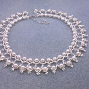 May include: A white pearl necklace with a delicate, intricate design. The necklace features small, white beads and a cascading pattern of pearls.