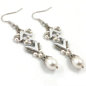 May include: Silver and white beaded earrings with a teardrop pearl dangle. The earrings feature a geometric design with small silver beads and clear crystals.
