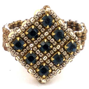 Könnte beinhalten: Ein quadratischer Ring mit einem geometrischen Design aus kleinen goldenen und silbernen Perlen. Die Mitte des Rings zeigt eine Ansammlung dunkelblauer Edelsteine.