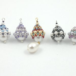 Könnte beinhalten: Sechs Perlenornamente in verschiedenen Farben, darunter Blau, Lila, Rot, Gold, Schwarz und Pink. Jedes Ornament ist mit einer Perle gekrönt und hat eine Schlaufe zum Aufhängen.