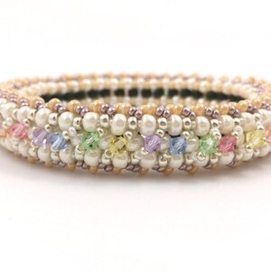 Può includere: Un braccialetto di perline bianche con un arcobaleno di piccole perline di cristallo.