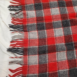 Op de afbeelding: Een rood, zwart en grijs geruite deken met gefranjerde randen. De deken heeft een klassiek ruitpatroon in tinten rood, zwart en grijs. De gefranjerde randen geven deze gezellige deken een decoratief tintje.