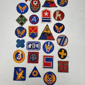 May include: A collection of vintage military patches in various shapes and colors. The patches feature emblems such as stars, wings, and geometric designs. The color palette includes blue, red, gold, and green.