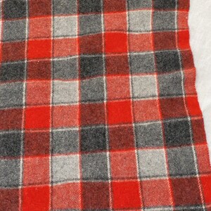 Op de afbeelding: Een rood, grijs en zwart geruite deken met gefranjerde randen. De deken heeft een klassiek vierkant patroon in tinten rood, grijs en zwart. De gefranjerde randen geven dit gezellige textiel een decoratief tintje.