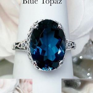 May include: A silver ring with a large, oval-shaped, blue topaz gemstone. The ring has a delicate, ornate design with small, white gemstones.