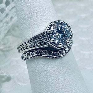 May include: A silver ring set with a large, clear, octagon-shaped gemstone. The ring has intricate floral designs on the band.