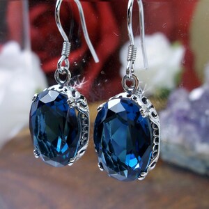 May include: A pair of silver dangle earrings with a large oval blue gemstone. The earrings have a delicate filigree design.