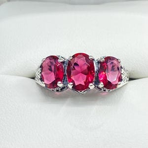 May include: A silver ring with three oval-shaped red gemstones. The ring has a delicate, ornate design.