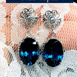 May include: A pair of silver earrings with a blue topaz stone. The earrings have a delicate floral design.
