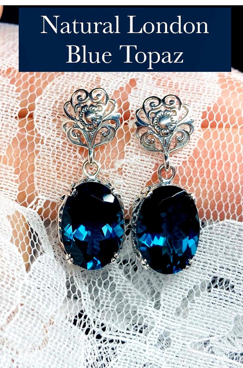 May include: A pair of silver earrings with a blue topaz stone. The earrings have a delicate floral design.