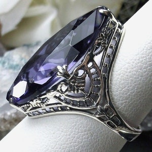 May include: A silver ring with a large, faceted, purple amethyst gemstone set in an intricate filigree design.