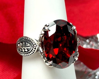May include: A silver ring with an oval-shaped red gemstone. The ring has a detailed design with a leaf pattern on the band.