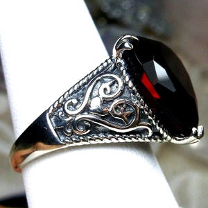 May include: A silver ring with an ornate design and a large, dark red gemstone.