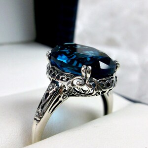 May include: A silver ring with an oval-shaped blue topaz gemstone set in a filigree design.