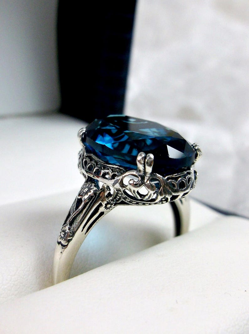 May include: A silver ring with an oval-shaped blue topaz gemstone set in a filigree design.