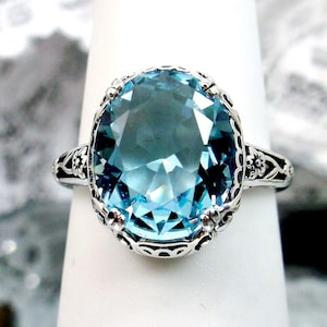 May include: A silver ring with a large, oval-shaped, light blue gemstone set in a filigree design.