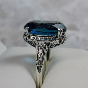 May include: A silver ring with a large, dark blue gemstone set in a filigree design.