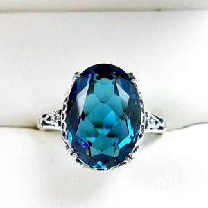May include: A silver ring with a large, oval-shaped, blue topaz gemstone. The ring has a delicate, filigree design.