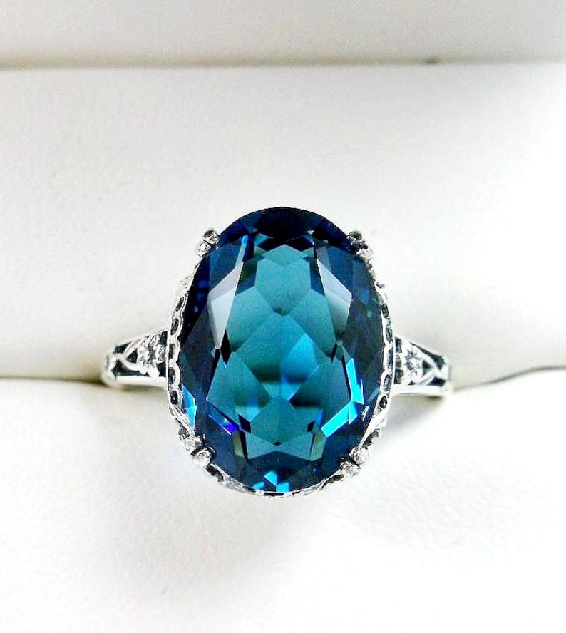 May include: A silver ring with a large, oval-shaped, blue topaz gemstone. The ring has a delicate, filigree design.
