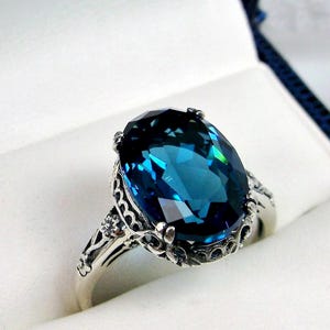 May include: A silver ring with an oval-shaped blue topaz gemstone set in a filigree design.