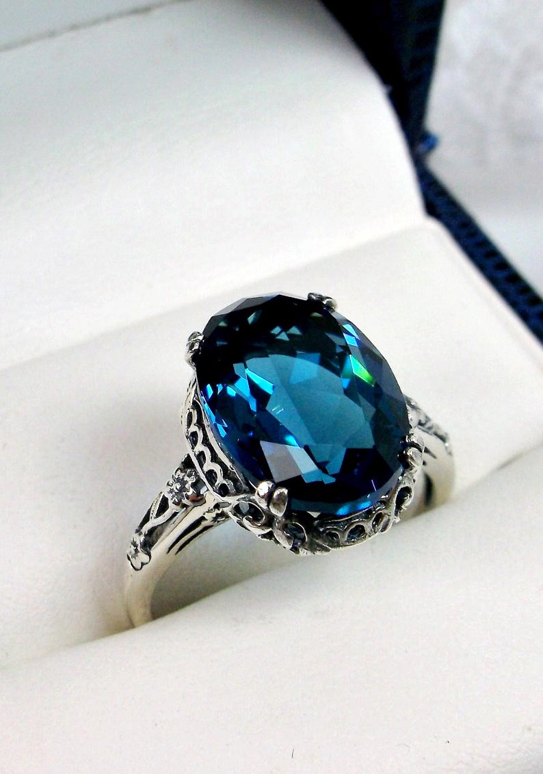 May include: A silver ring with an oval-shaped blue topaz gemstone set in a filigree design.
