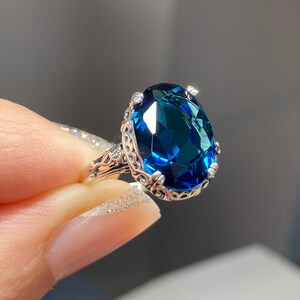 May include: A silver ring with a large, oval-shaped, dark blue gemstone set in a filigree design.