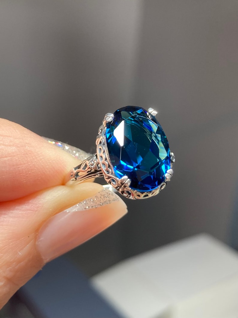May include: A silver ring with a large, oval-shaped, dark blue gemstone set in a filigree design.