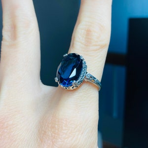May include: A silver ring with a large, oval-shaped, dark blue gemstone set in a decorative, filigree-style band.